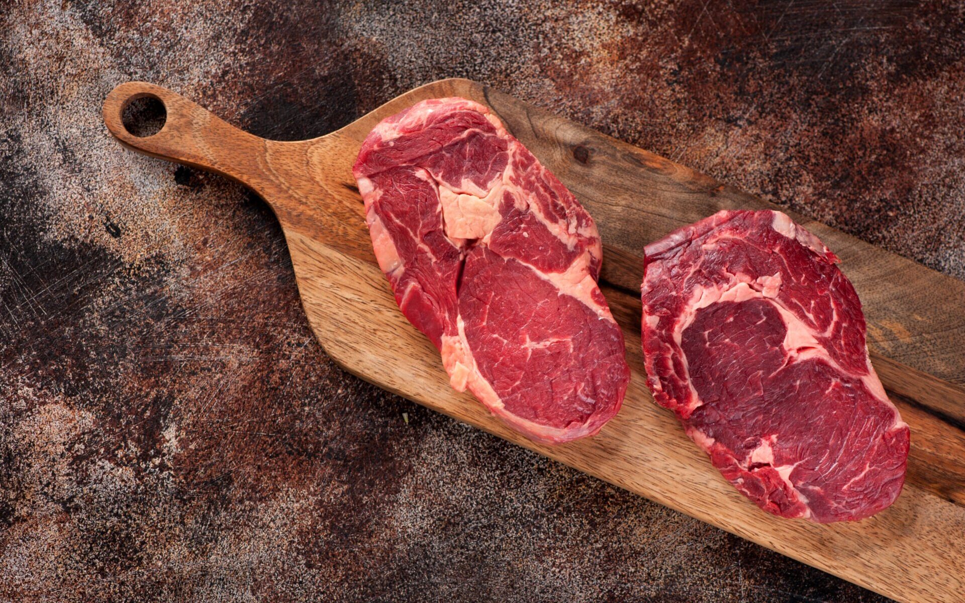Raw ribeye steak on a wooden board, top view